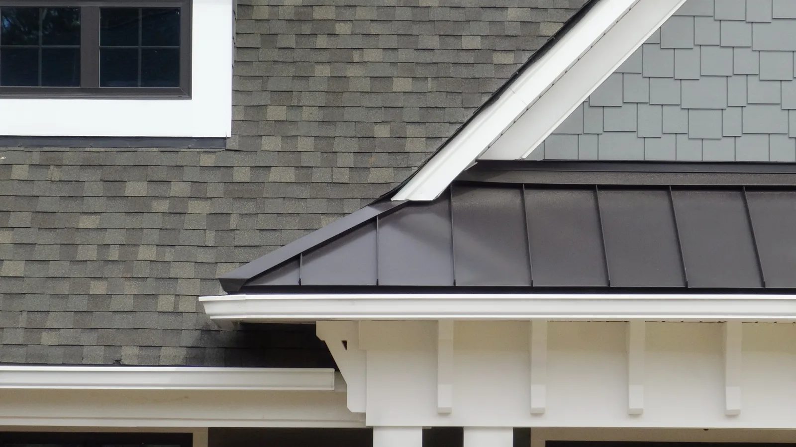 Gray shingle roof meeting a dark standing seam roof with white trim